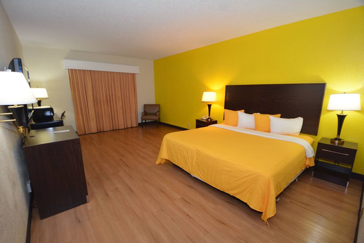 A hotel room with a large bed, wooden floor, a desk with a lamp, and a chair.