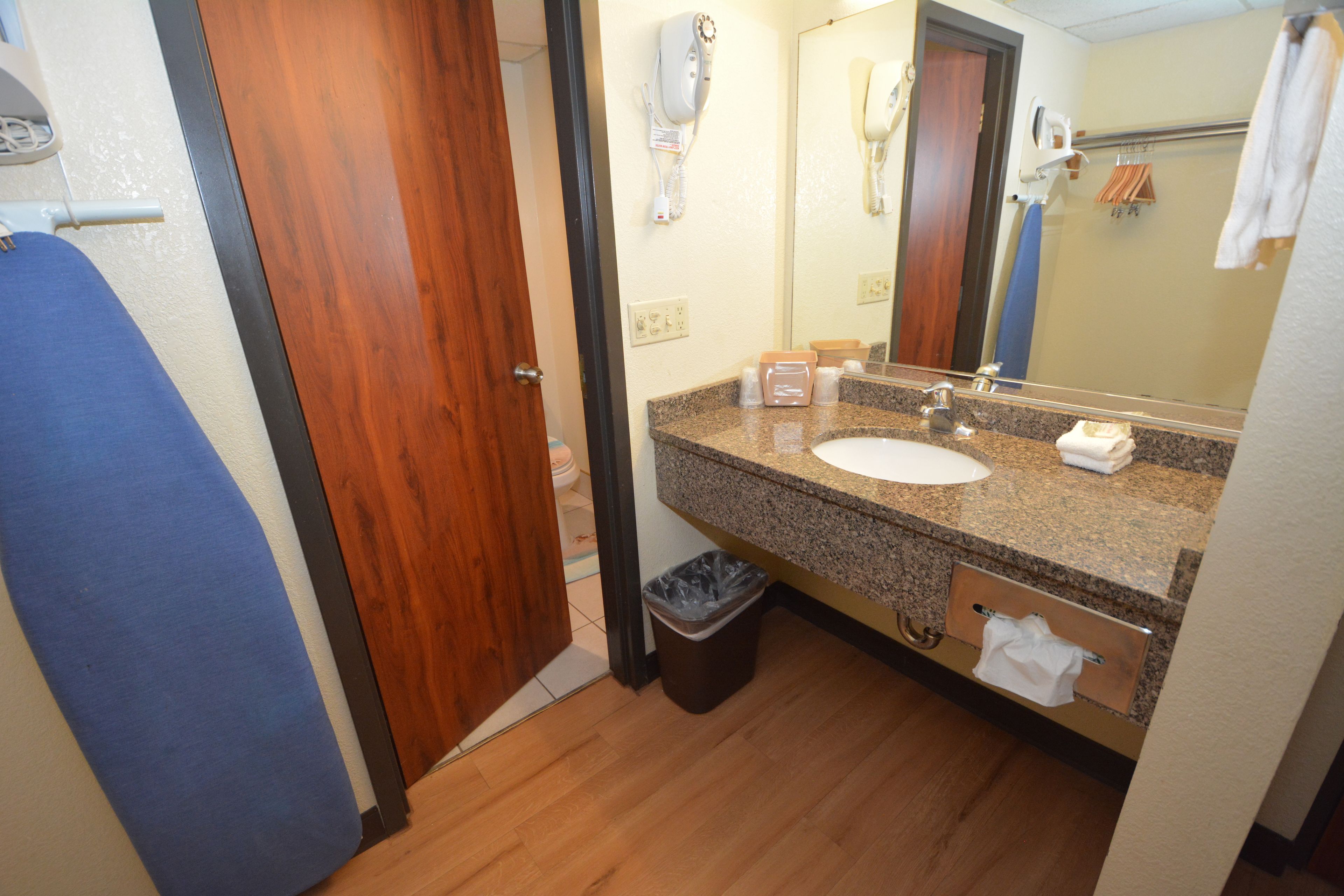 Un baño con puerta de madera, un lavamanos, un espejo y un secador de pelo montado en la pared.