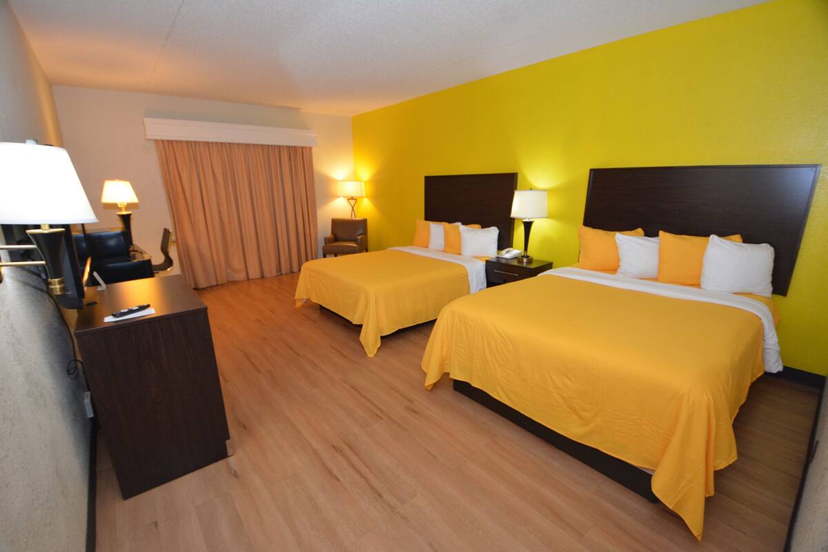 A hotel room with two beds, wooden flooring, a desk, and lamps.