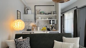A modern living room with a dark grey sofa, white and patterned cushions, a hanging light fixture, and a kitchen area with white cabinets, a microwave, and various kitchen items. - B-Cozy 1-bedroom apartment in enjoyable Istanbul with WiFi, AC (İstanbul)