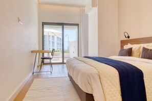 Ein Schlafzimmer mit Bett, Sessel, Schreibtisch und Blick ins Freie.