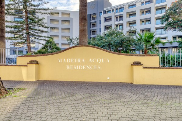 Schild für Madeira Acqua Residences mit befestigter Auffahrt und umliegendem Grün.