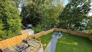 A backyard with a wooden deck, outdoor seating, and a grassy lawn.