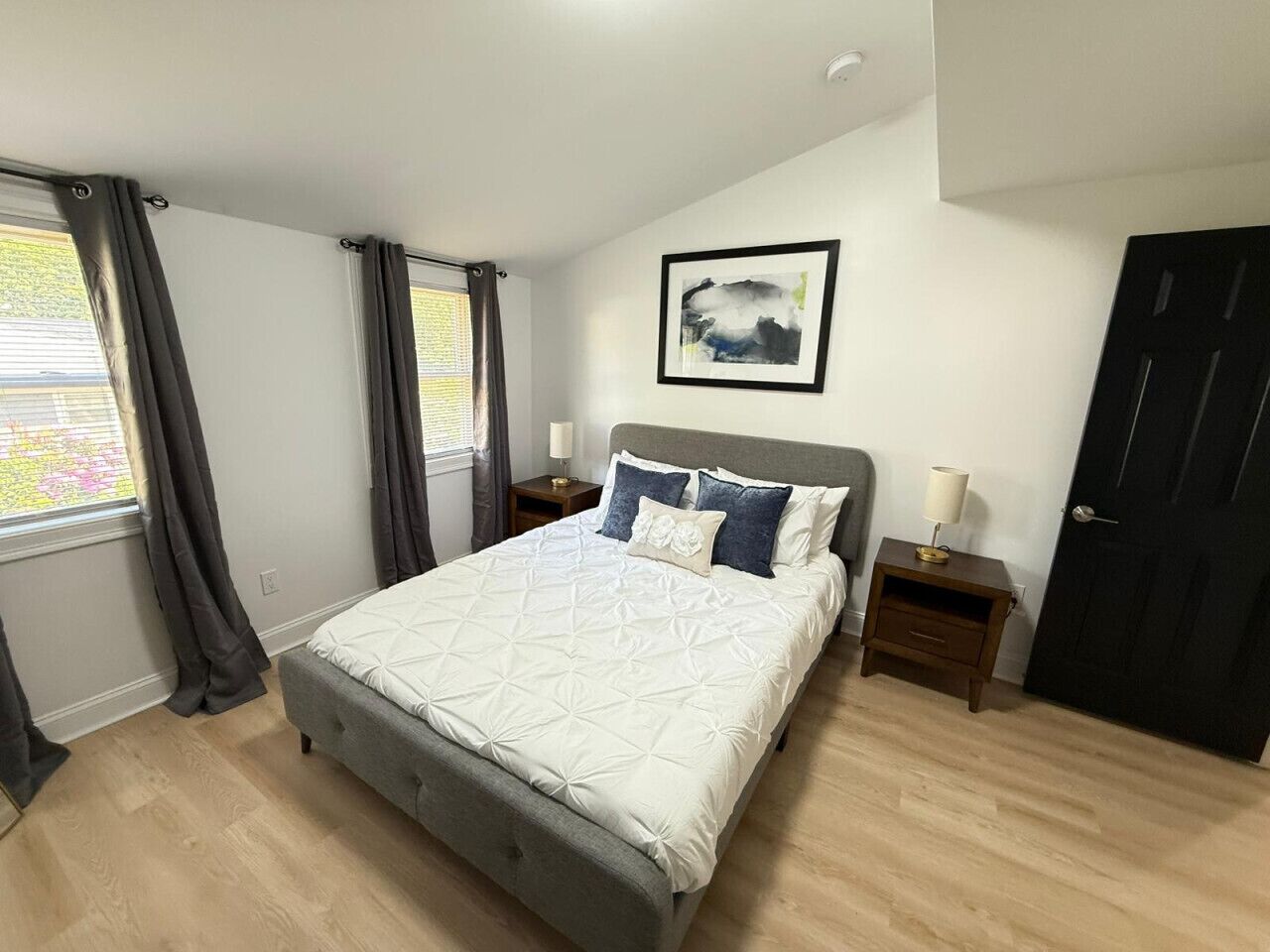 Une chambre à coucher avec un lit, des tables de chevet, une porte et une fenêtre avec des rideaux.