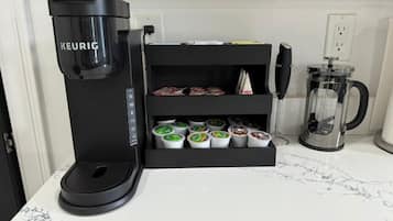 A coffee machine with a coffee pod holder below it, a glass carafe, and a power outlet on the wall.