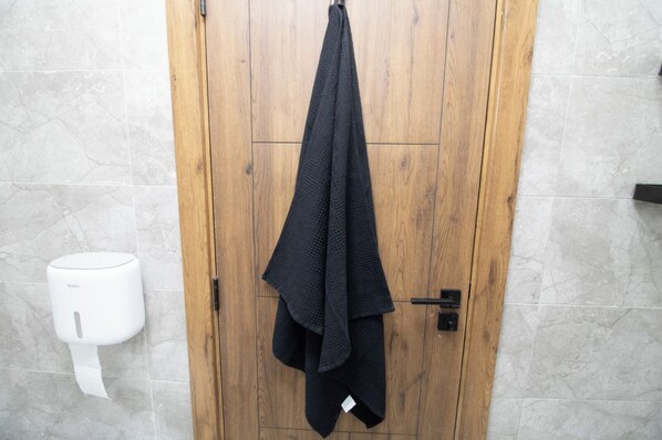 A wooden door with a towel hanging on a hook, a white towel dispenser, and a tiled wall.