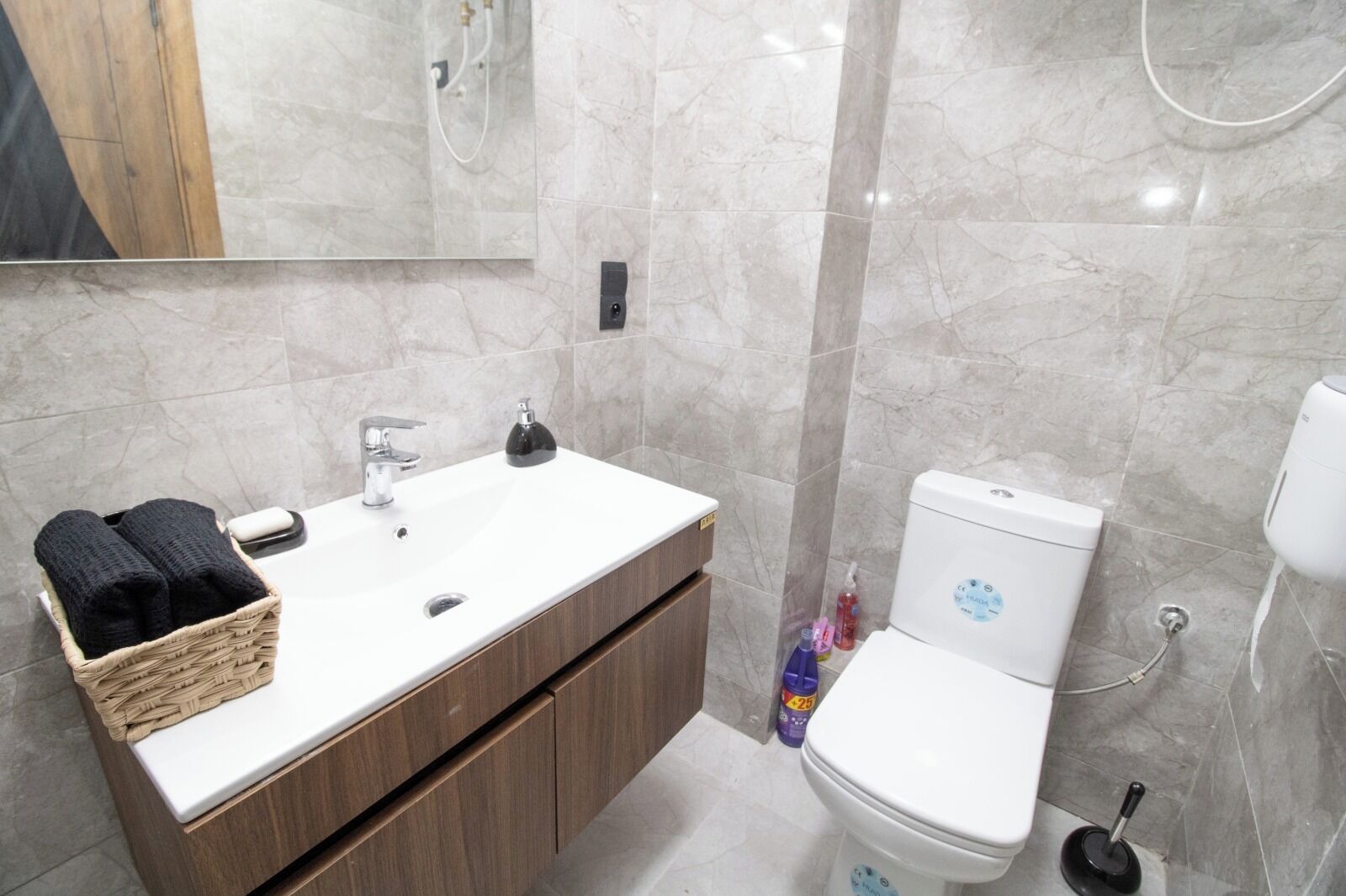 A bathroom with a white sink, wooden cabinets, a toilet, and a mirror.