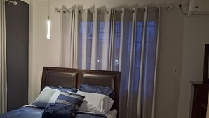 Een slaapkamer met een bed, een plafondventilator, een raam met gordijnen en een airconditioning.