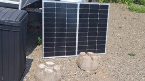 A solar panel system installed on a trailer with a white storage container and a white plastic chair. - Cozy Camper setup, off grid (Dunlop)