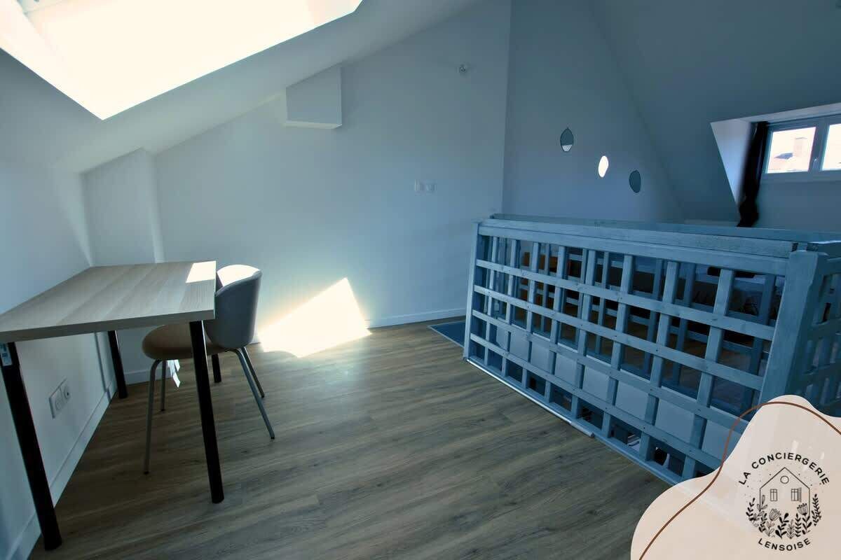 A room with a skylight, a dining table with chairs, a blue crib, and a logo on the crib.