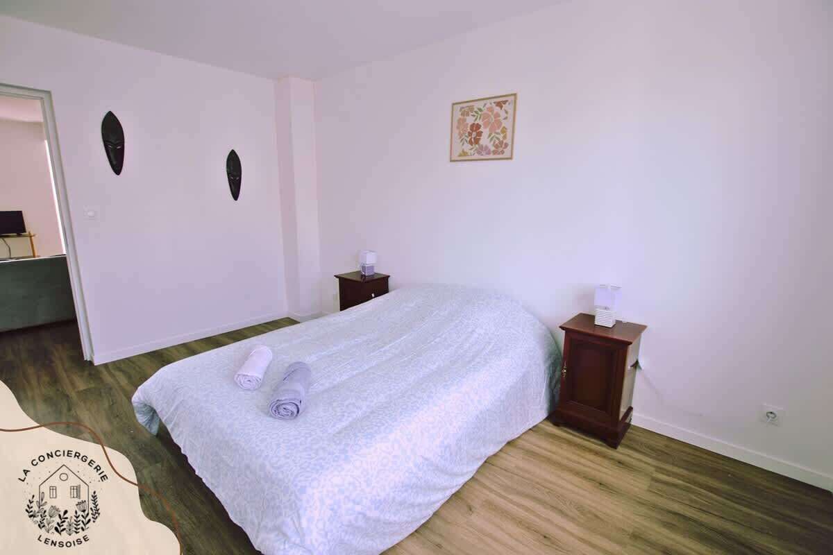 Un dormitorio con una cama, dos mesitas de noche, una pequeña mesa con lámpara y una puerta.
