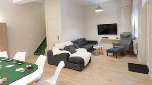 Una sala de estar moderna con una mesa de póker verde, un sofá gris, un televisor y una escalera.