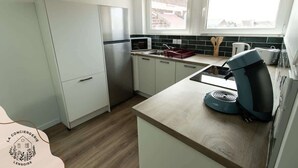 Una cocina moderna con armarios blancos, un refrigerador de acero inoxidable, un microondas y una cafetera en la encimera.