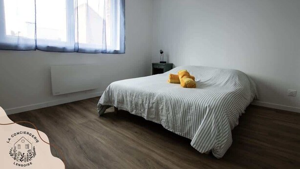 Un dormitorio con cama, mesita de noche, ventana con cortinas y radiador.