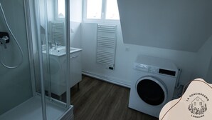 Un baño moderno con cabina de ducha de vidrio, un lavamanos y lavadora integrada.