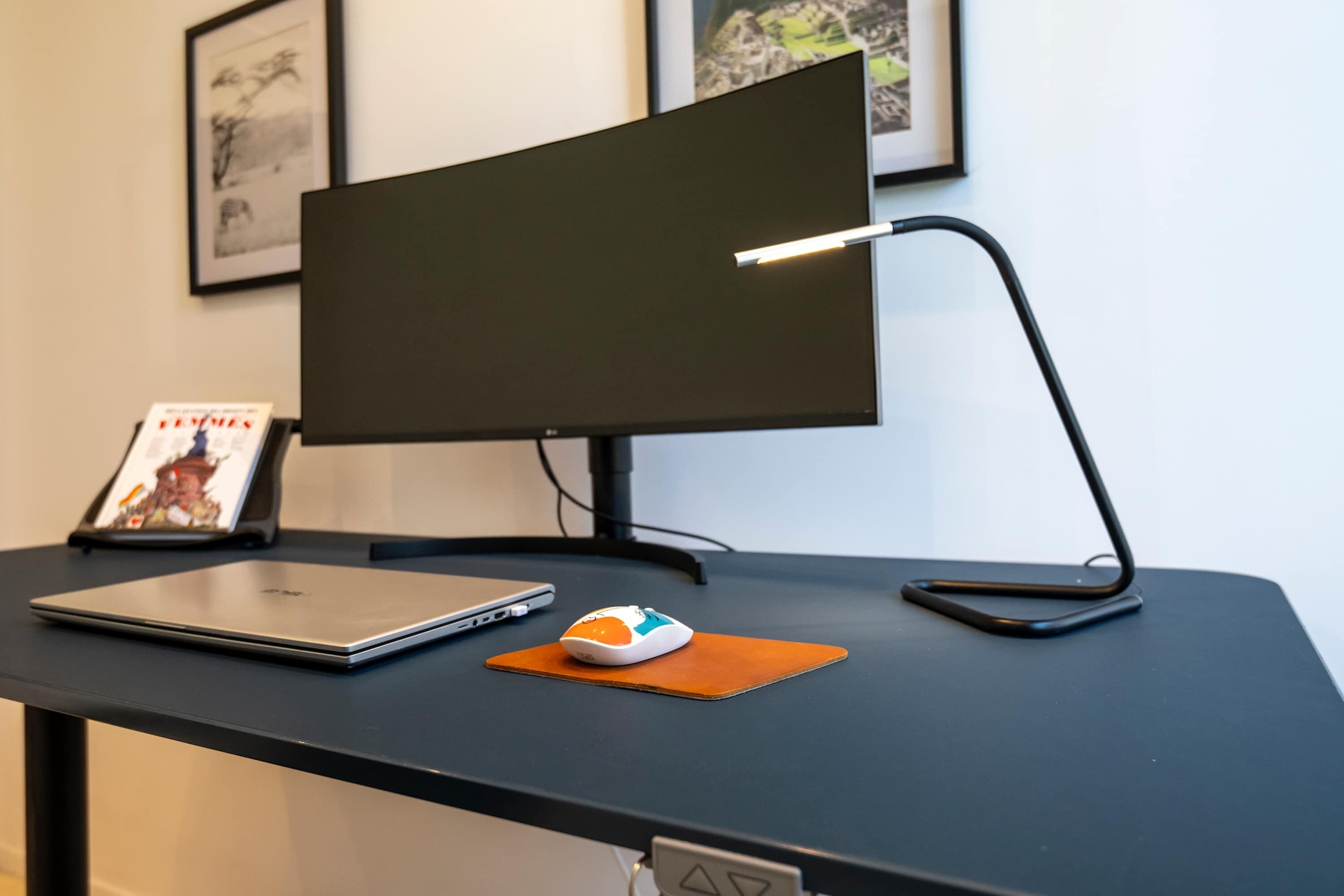 Un bureau avec un ordinateur portable, une souris, un écran et un cadre contenant une photo.