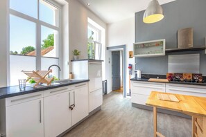Una cocina moderna con armarios blancos, una encimera de madera y vistas al exterior gracias a amplios ventanales.