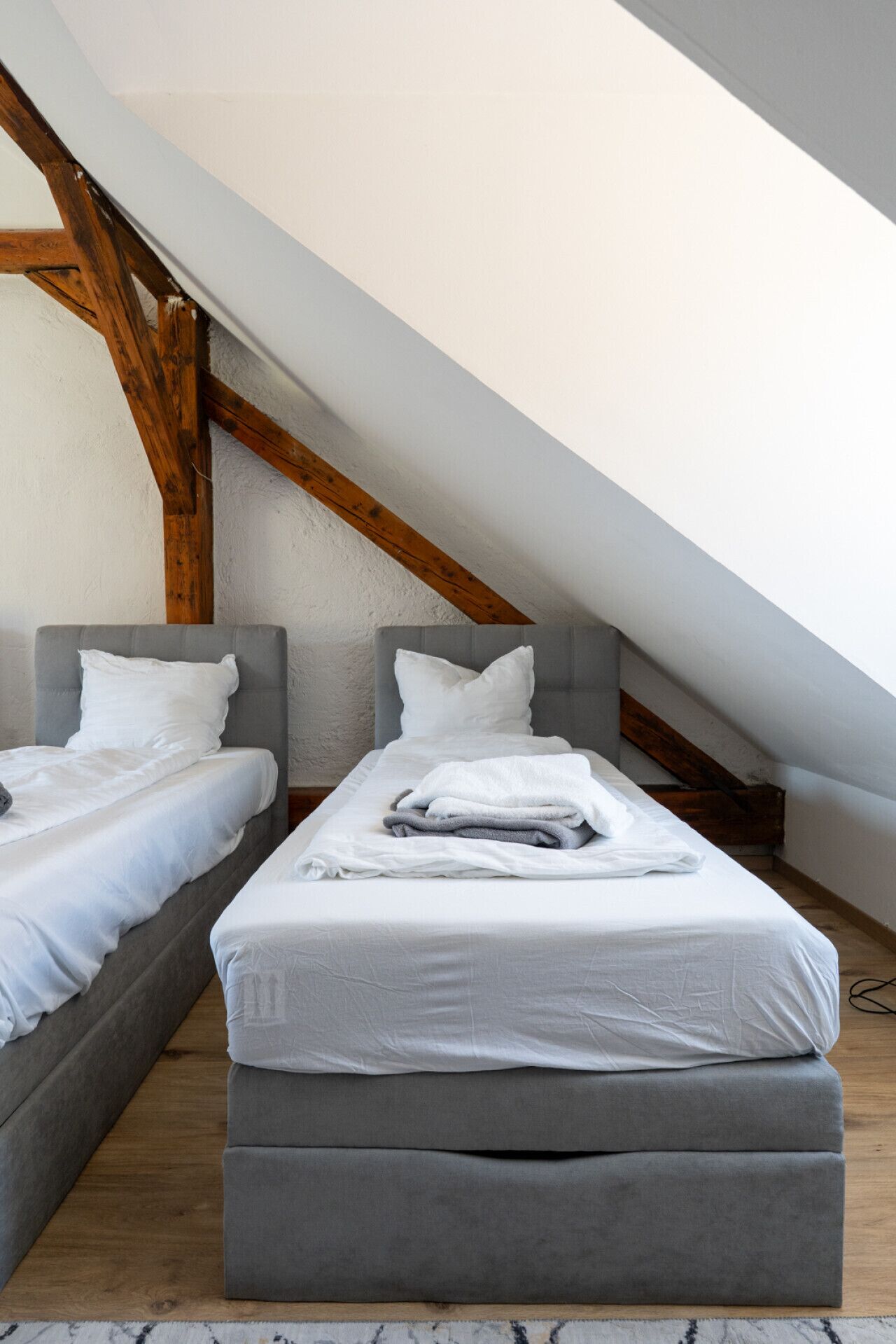 A bedroom with two beds, wooden beams, and a sloped ceiling.