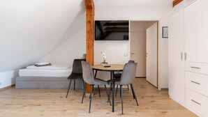 A small, modern room with a loft bed, a dining table with chairs, and a white wardrobe.