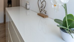 A clean, modern reception area with a white counter, a potted orchid, a heart-shaped metal decoration, and a framed artwork on the wall.