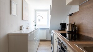 A narrow kitchen with a window, a radiator, a coffee maker, and a kettle.