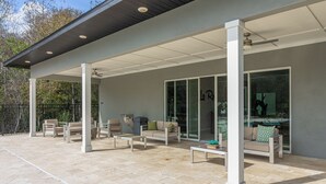 A covered patio area with outdoor furniture, including sofas and chairs, and a glass door leading to a pool. - Luxury Townhome near attractions! (Kissimmee)