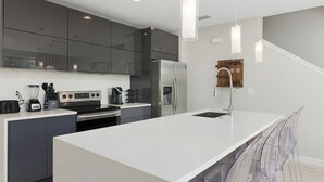 A modern kitchen with a large island, stainless steel appliances, and clear plastic chairs. - Luxury Townhome near attractions! (Kissimmee)