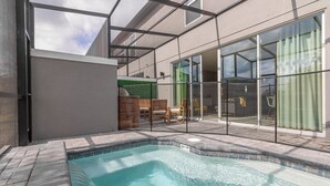 A swimming pool with a tiled edge, a wooden deck, and a glass door leading to a covered patio area. - Luxury Townhome near attractions! (Kissimmee)