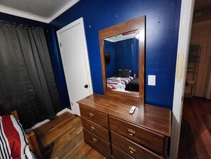 Una stanza con un comò in legno, un letto con copripiumino a righe, una porta bianca e pareti blu.