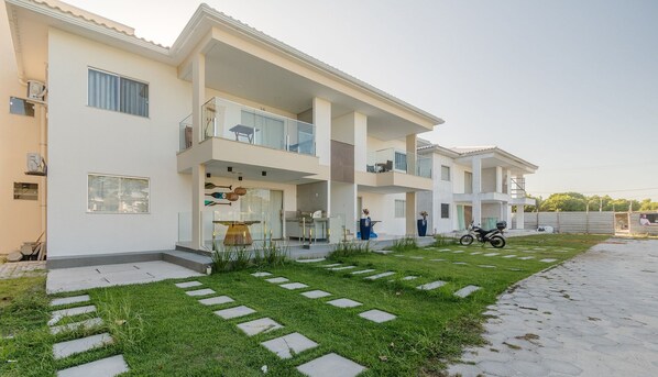 A multi-story residential building with a balcony, a paved driveway, and a motorcycle parked outside. - Condominium With Swimming Pool at Praia do Muta in Porto-ba - MUT (Porto Seguro)