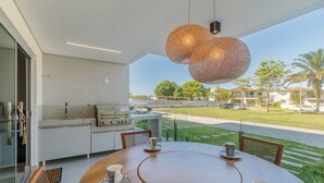 Uma área de refeições moderna ao ar livre, com uma mesa redonda, cadeiras e uma luminária suspensa diferenciada.