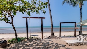 Uma praia com baloiço, espreguiçadeira e guarda-sol.
