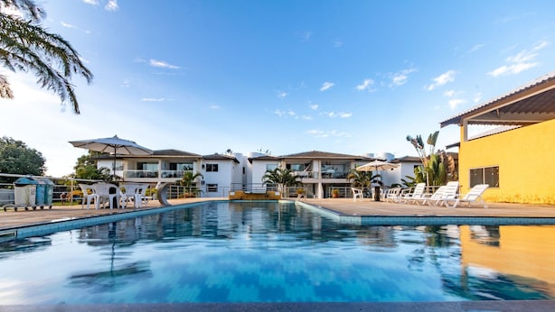 Piscina com espreguiçadeiras e guarda-sóis, cercada por edifícios com varandas.