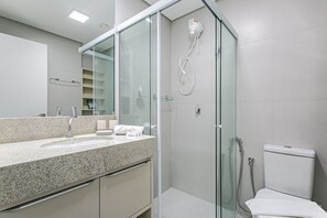 Ein modernes Badezimmer mit einer gläsernen Duschkabine, einem Waschbecken mit Marmorplatte und einer Toilette.