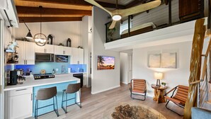 Una cocina moderna con barra, vigas de madera en el techo y un dormitorio en loft superior.