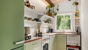 A kitchen with a stove, oven, microwave, and sink. There are shelves with dishes and a plant hanging from the ceiling. - Amazing home in Melby with sauna (Melby)