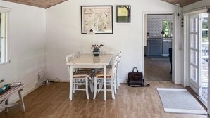 Un coin repas avec une table en bois et des chaises blanches, une carte accrochée au mur et une vue sur la cuisine.