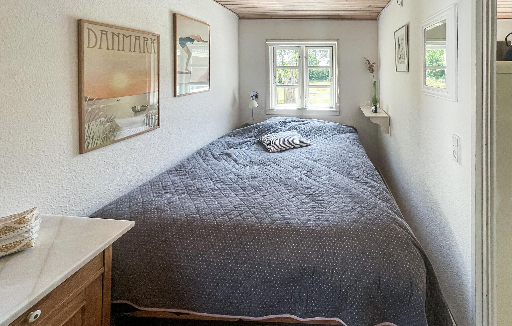 A bedroom with a bed, a dresser, a window, and wall art.