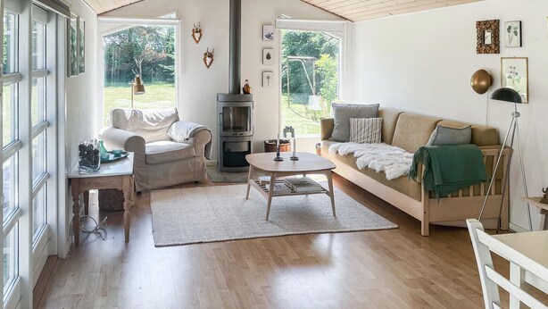 Un salon chaleureux avec un canapé, une table basse et une cheminée. Deux fenêtres laissent entrer la lumière naturelle et offrent une vue sur l’extérieur.