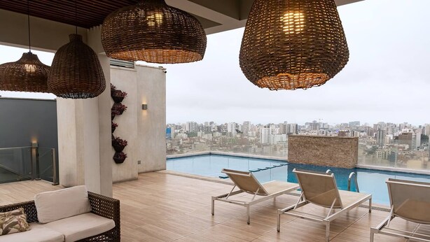 A rooftop terrace with a pool, lounge chairs, and wicker pendant lights.