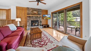 A living room with a stone fireplace, a ceiling fan, a red sofa, a wooden coffee table, and a large sliding glass door leading to an outdoor patio.