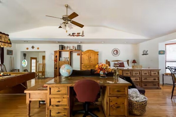 A spacious living room with a pool table, wooden furniture, a globe, and a ceiling fan.