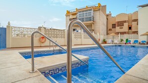 Una piscina con borde de mosaico azul, barandillas de metal y un flotador salvavidas.