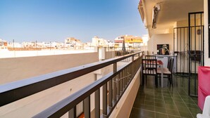 Un balcón con vistas a la ciudad, una mesa con sillas y una pequeña cocina con pileta y placares.