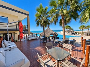 A deck with outdoor seating, a pool, and a view of the beach.