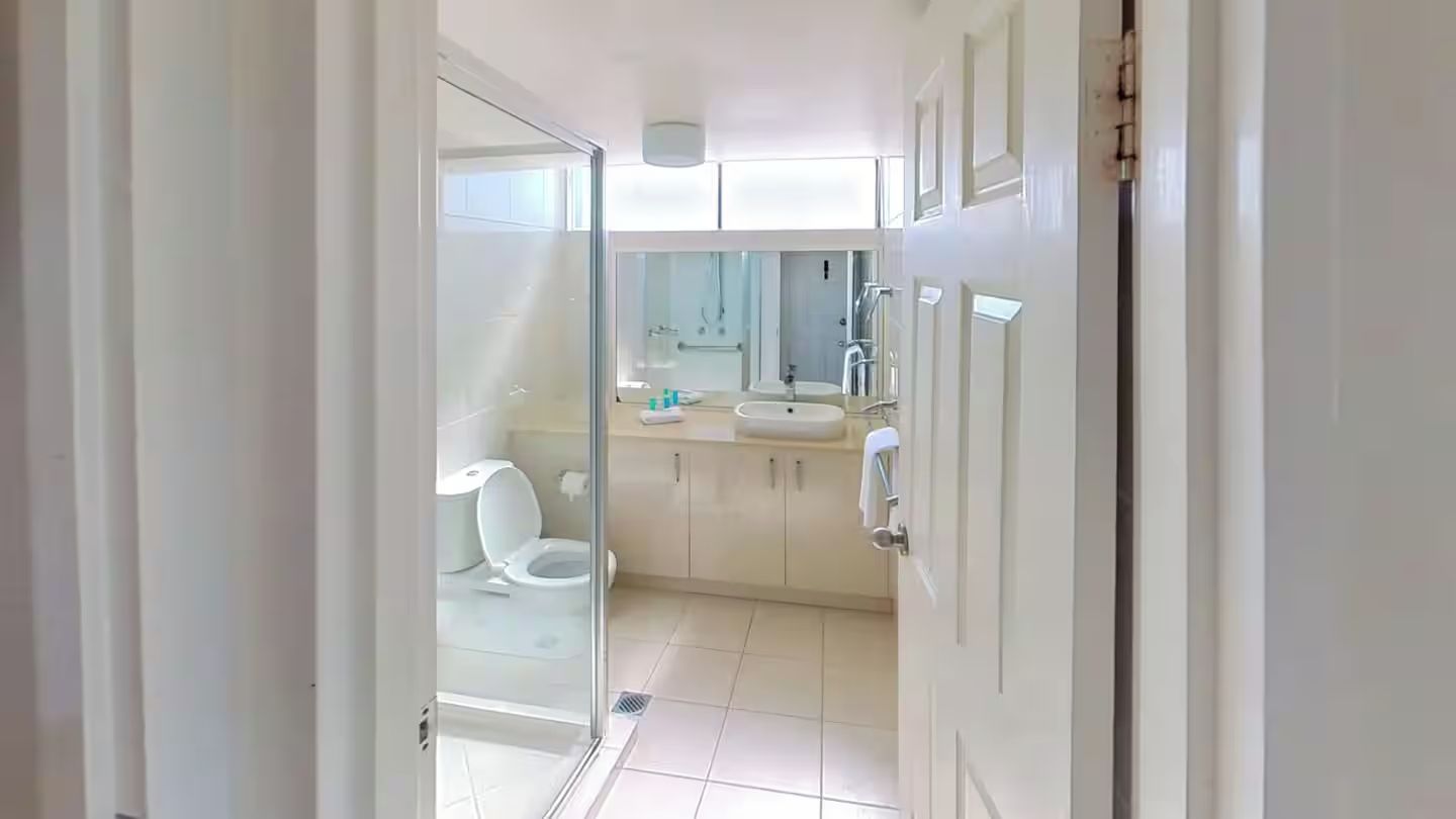 A narrow hallway leading to a bathroom with a toilet, sink, and shower.