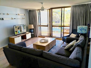 A living room with a sofa, a coffee table, a TV, and a sliding glass door leading to an outdoor area.