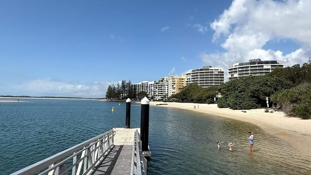 A pier leading to a beach with a clear view of a coastal cityscape in the background. - Gemini Resort - Unit 19 (Golden Beach)