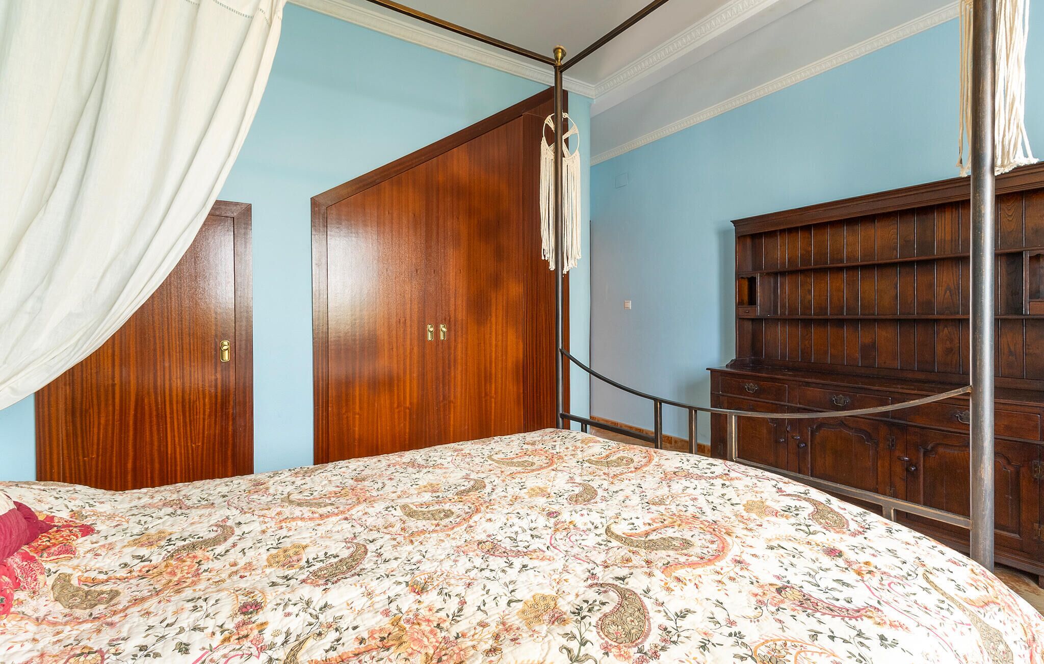 A bedroom with a large bed, a wooden wardrobe, and a chest of drawers.