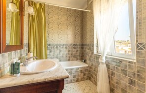 Une salle de bain avec un lavabo blanc, une baignoire et une fenêtre donnant sur des immeubles.